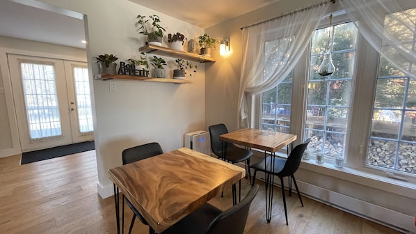 Zona de menjador amb taula i cadires de fusta, un refrigerador petit i plantes en testos sobre prestatges.