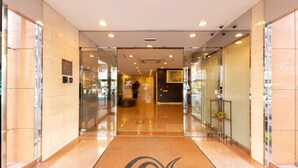 A modern hotel lobby with a glass entrance, a reception desk, and a clear view of the street outside. - Nishitetsu Inn Shinsaibashi (Osaka)
