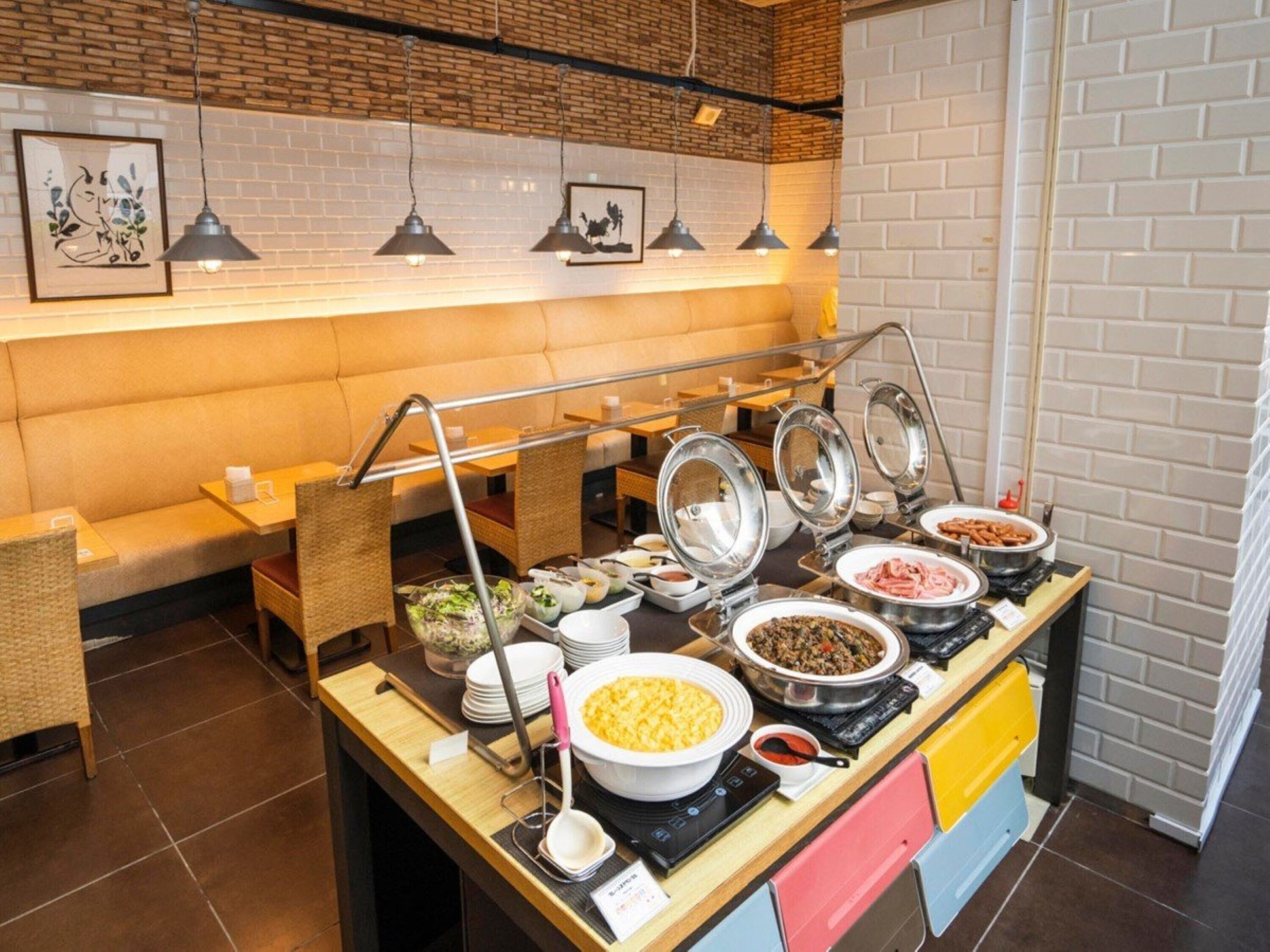 A buffet setup with various food items, a seating area with a bench, and a brick wall with framed artwork.