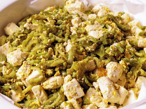 A close-up of a dish with green beans and chunks of chicken.