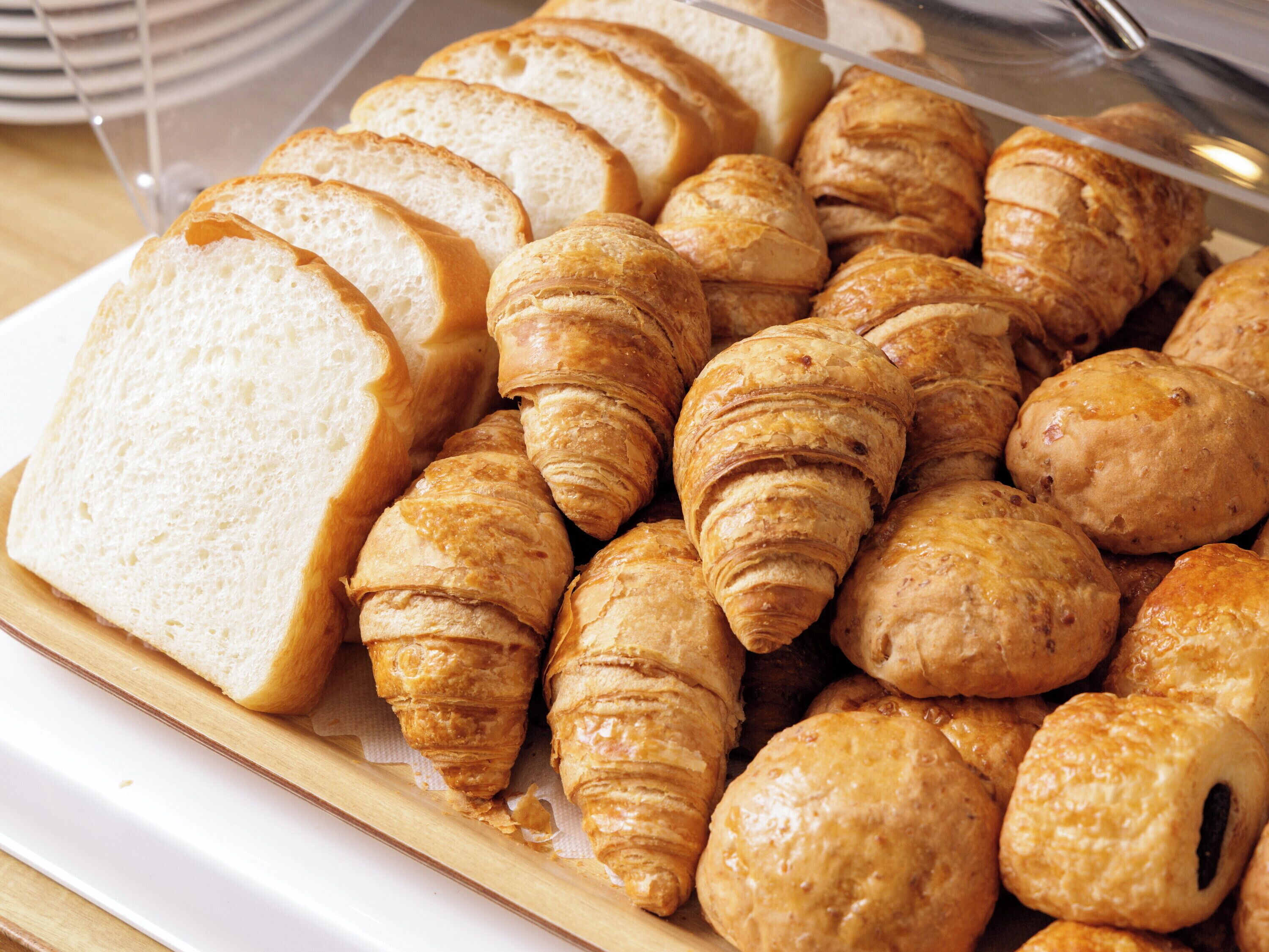 Variedad de panes y pasteles, incluyendo pan en rebanadas y croissants, expuestos sobre una tabla de madera.