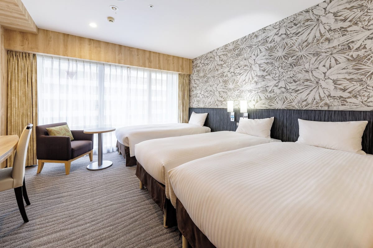 A hotel room with two beds, a desk, a chair, and a large window with curtains.