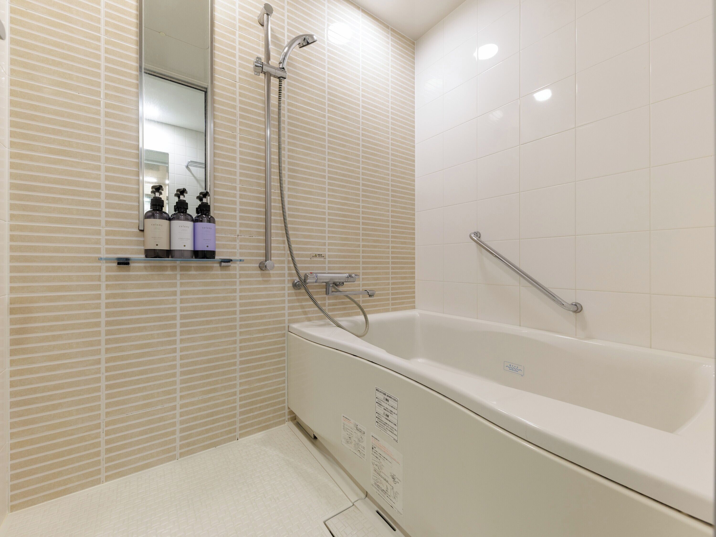 A modern bathroom with a white bathtub, a handheld showerhead, and a glass shelf with toiletries.