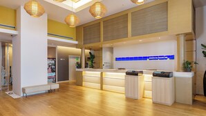 Zona de recepción de hotel con suelo de madera, un mostrador de recepción y tres lámparas colgantes de mimbre.