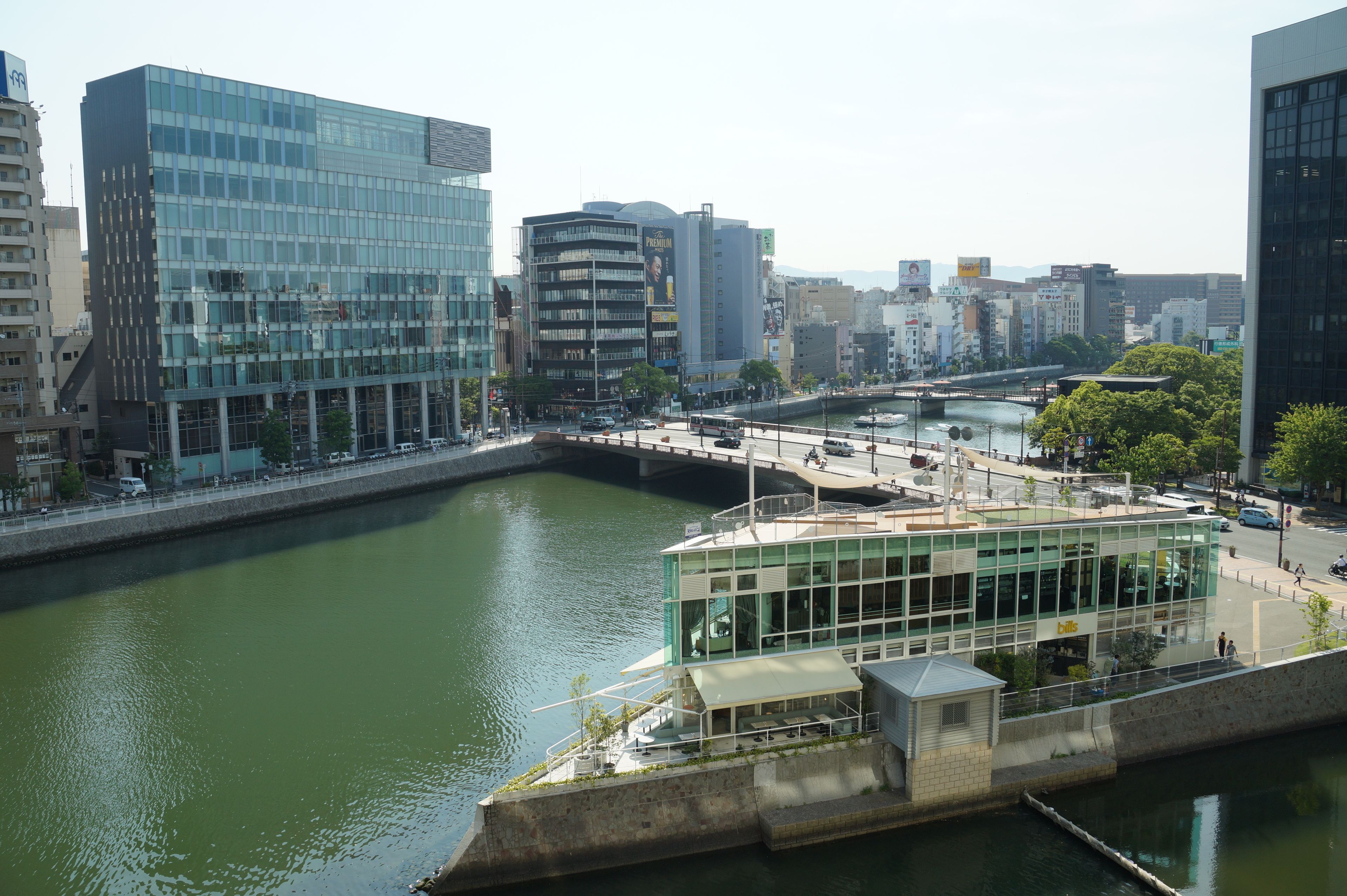 Une vue sur la ville, avec ses bâtiments modernes, un pont et un restaurant doté d’une terrasse, le tout surplombant la rivière.