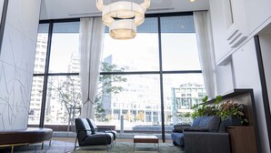 A modern lobby with large windows, a black leather sofa, a grey sofa, a wooden coffee table, and a hanging light fixture. - Nishitetsu Inn Fukuoka (Fukuoka)
