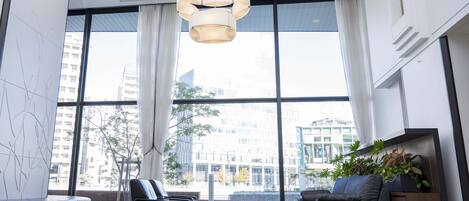 A modern lobby with large windows, a black leather sofa, a grey sofa, a wooden coffee table, and a hanging light fixture.