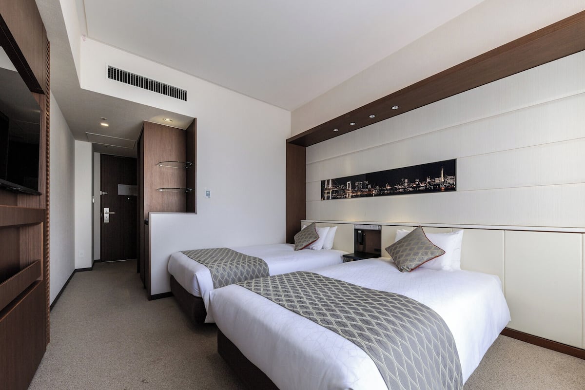 Habitación de hotel con dos camas, vistas a la ciudad, televisor y armario de madera.