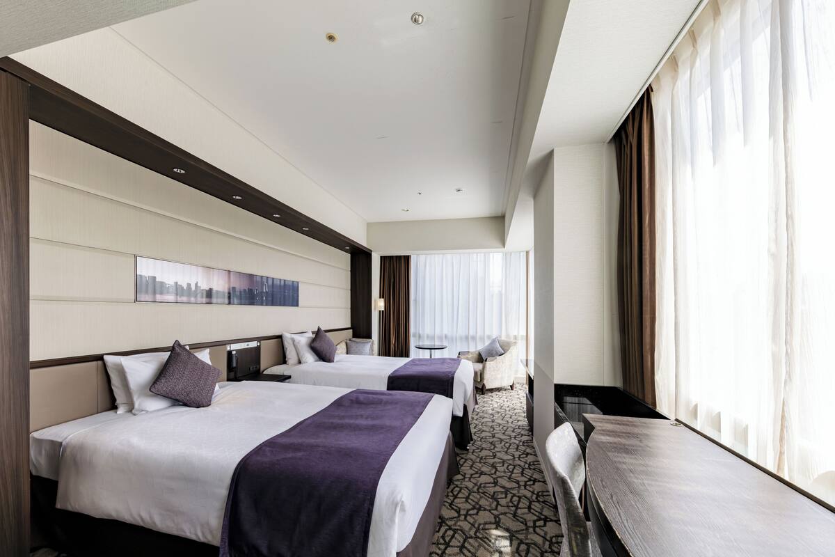 Habitación de hotel con dos camas, un escritorio y un ventanal grande con cortinas.