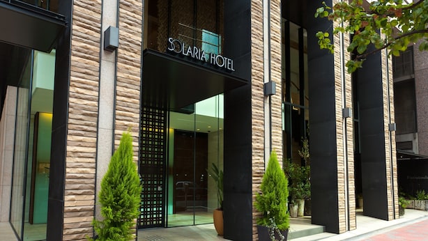 The exterior of Solaria Hotel with a modern facade, large glass entrance, and potted plants in front. - Solaria Nishitetsu Hotel Ginza (Tokyo)