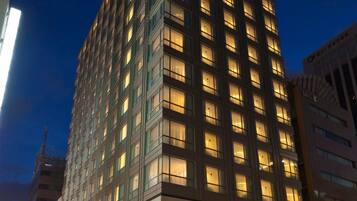 Experience the hotel's inviting corner entrance with a grid of windows and warm interior lighting.