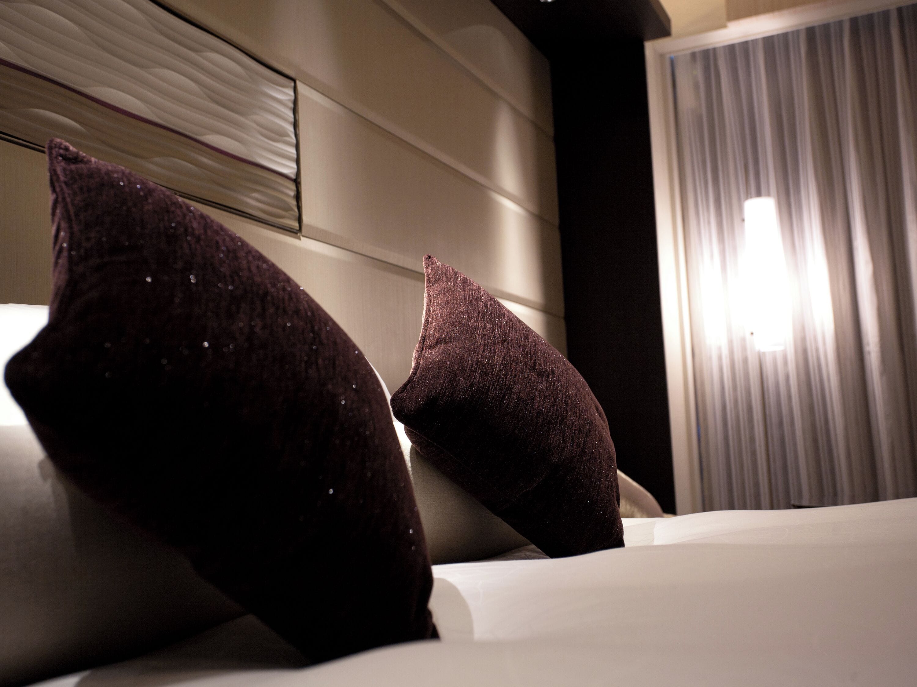 A bed with two dark pillows and a white headboard in a hotel room.