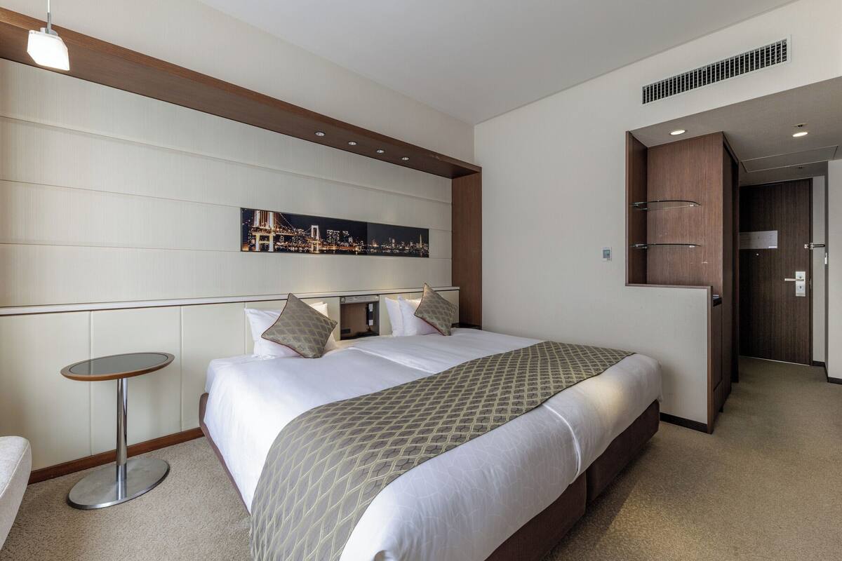 Habitación de hotel con una cama grande, una mesita redonda, una obra de arte con un paisaje urbano en la pared y un armario.