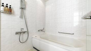 A modern bathroom with a bathtub, a shower with a handheld showerhead, and a shelf with toiletries.