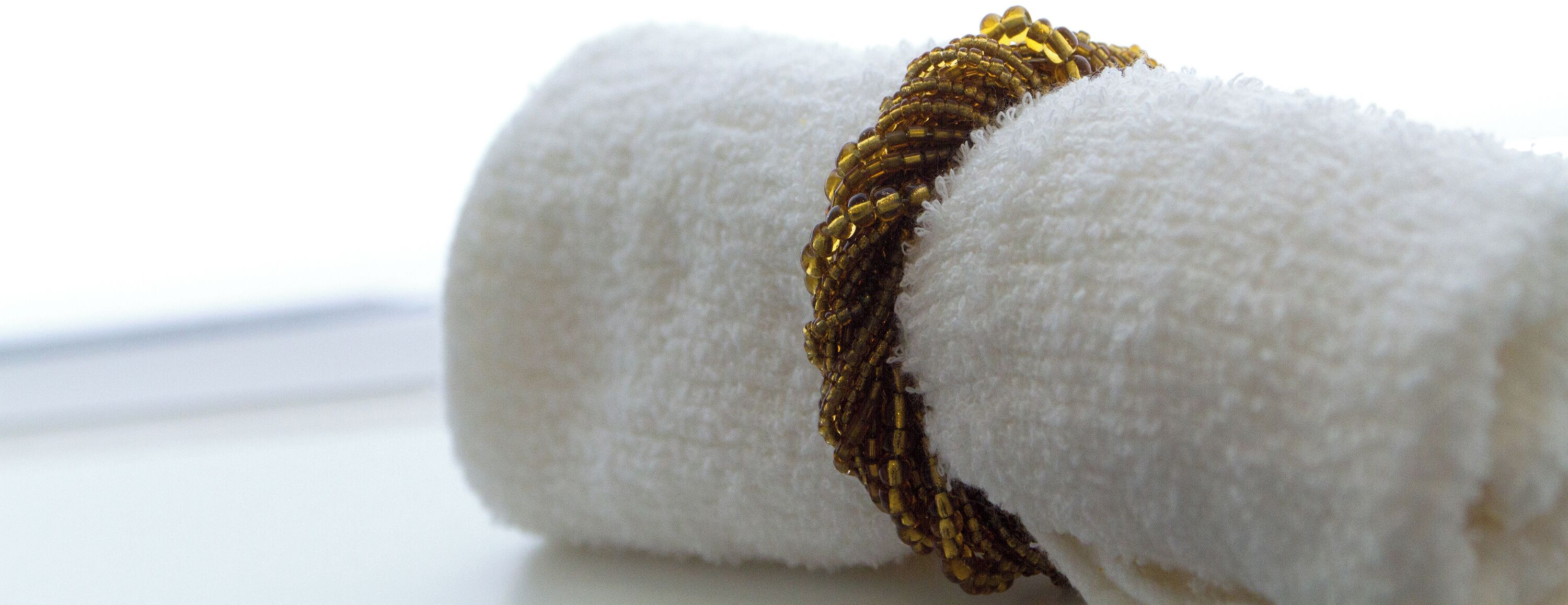 A white towel with a gold-colored beaded bracelet.