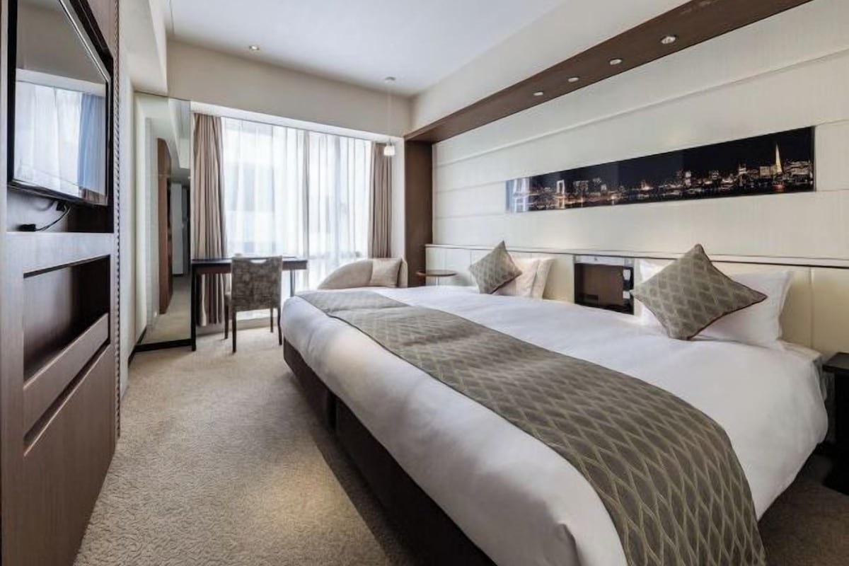 A modern hotel room with a large bed, a flat-screen TV, a desk, and a cityscape view.