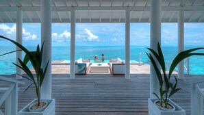 Un espacio exterior techado con piscina, dos personas relajándose y vista al océano.