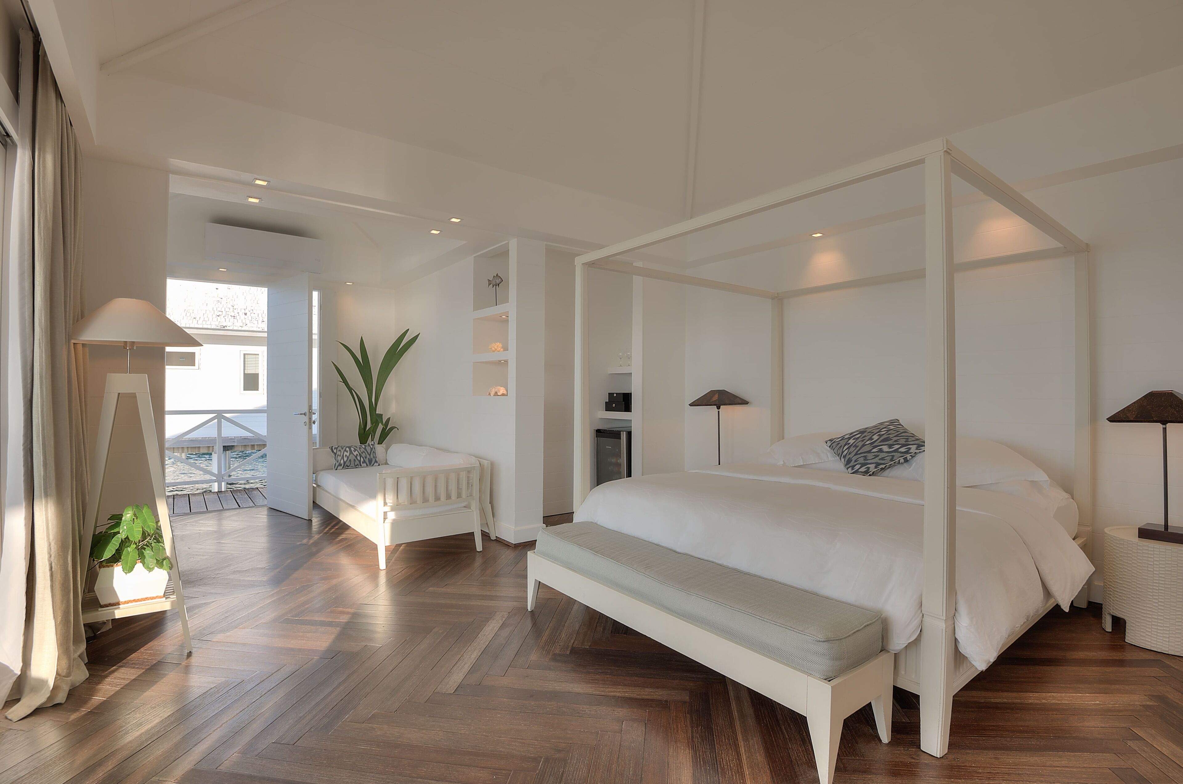 A spacious bedroom with a four-poster bed, a bench, and a bedside table with lamps.