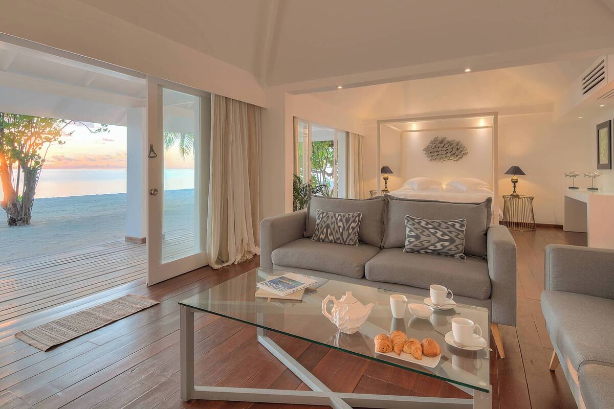 A modern living room with a glass coffee table, a grey sofa, and a view of the sea.