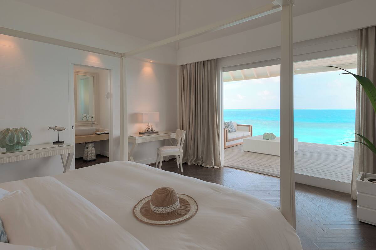 A hotel room with a bed, a desk, a chair, a view of the ocean, and a balcony.
