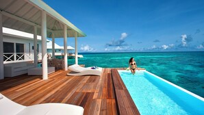Una terraza de madera con piscina, sillones de descanso y un área de estar cubierta con vistas al océano.