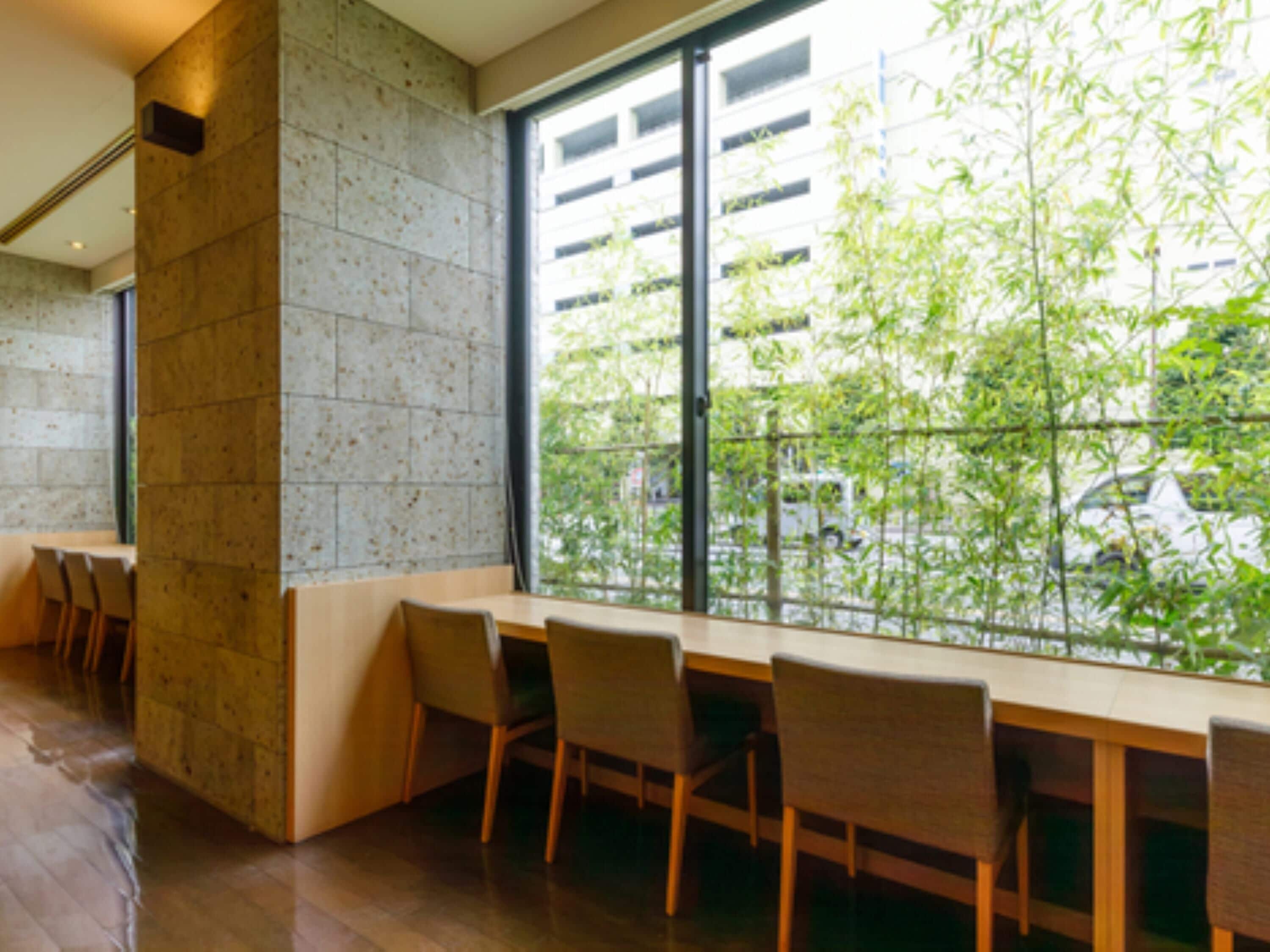 A modern interior with a long table and chairs, a stone wall, and a large window overlooking greenery.