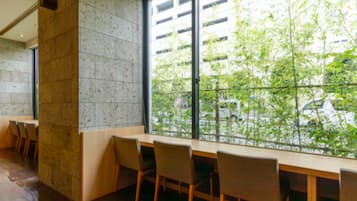 A modern interior with a long table and chairs, a stone wall, and a large window overlooking greenery.