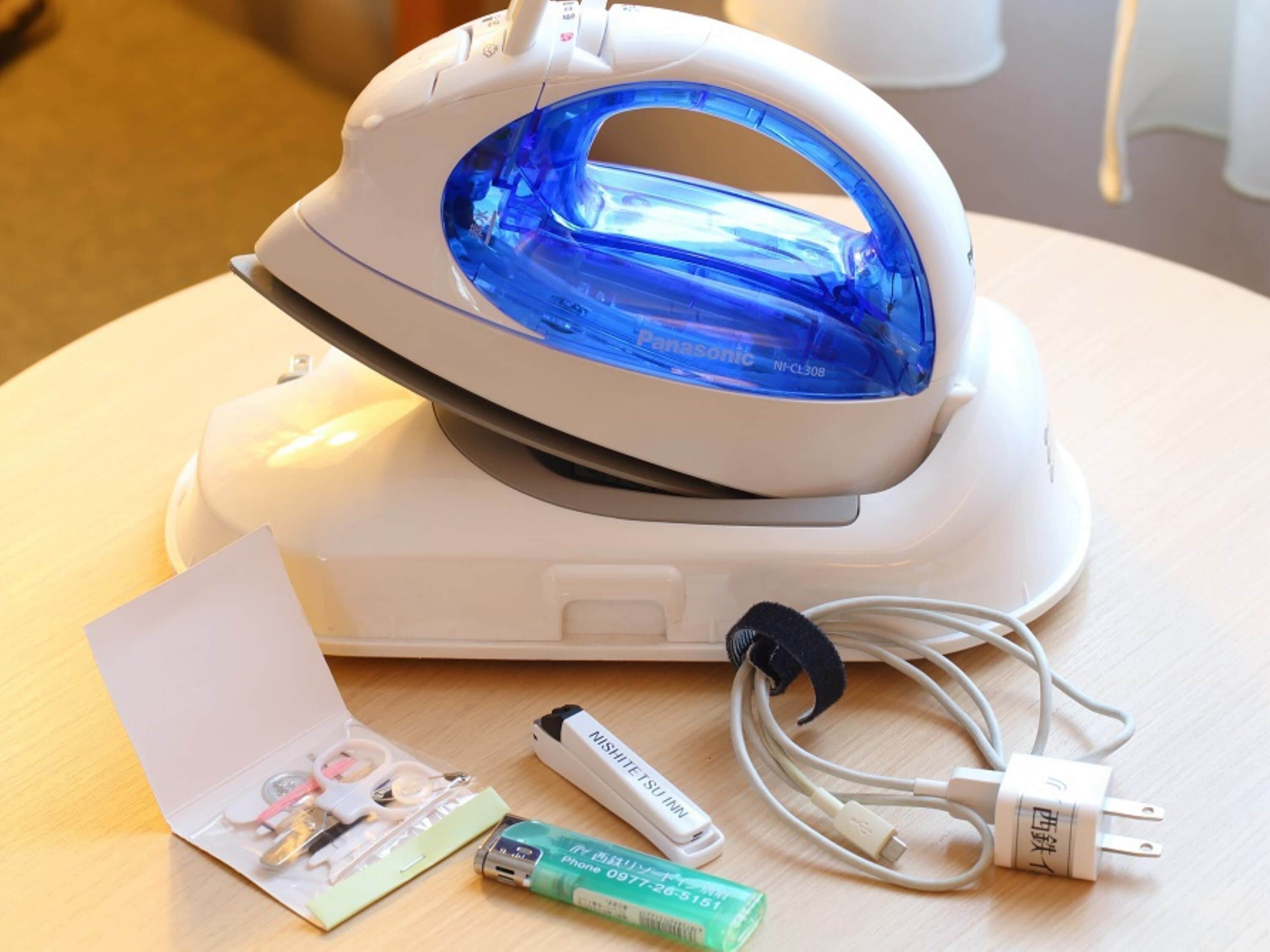 Una plancha blanca con interior azul, un adaptador de corriente, un cable USB y un pequeño folleto sobre una superficie de madera.