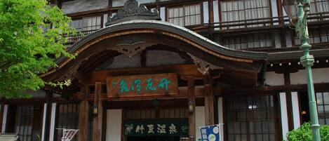 A traditional Japanese building with a wooden facade, a signboard with Japanese characters, and a red post box.