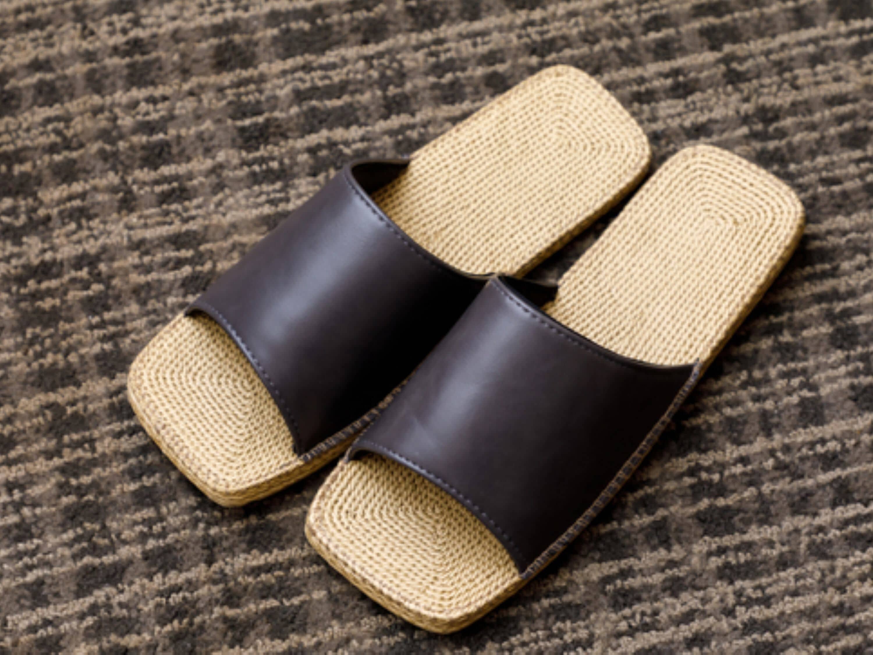 A pair of black leather sandals with woven soles on a textured carpet.