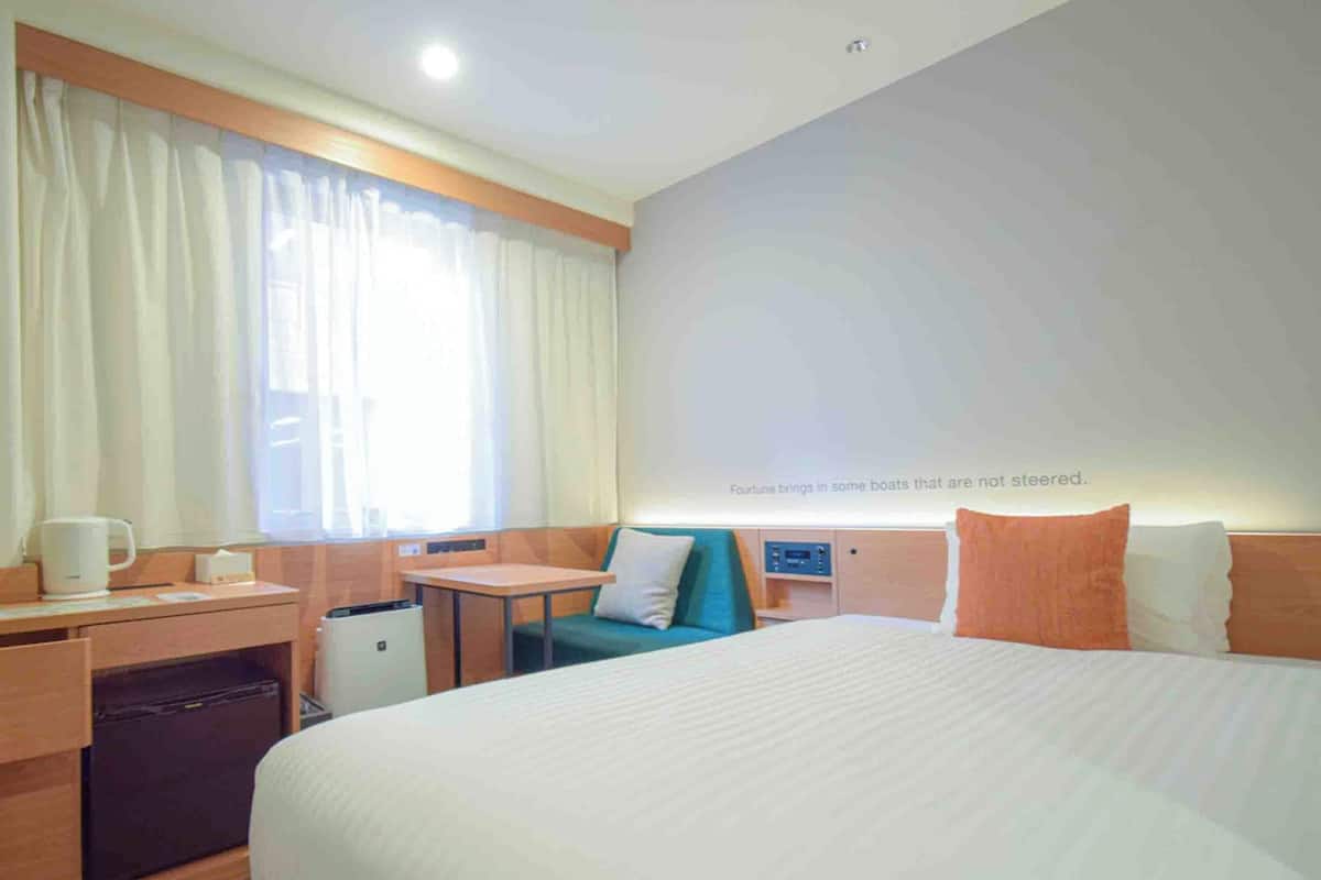 A hotel room with a large bed, a desk, a chair, a small table, and a window with curtains.