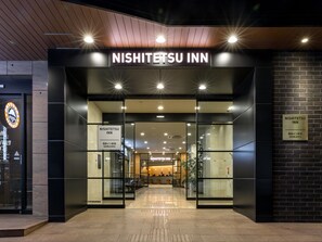 L’extérieur du NISHITETSU INN présente un design moderne, avec des portes en verre et une enseigne au-dessus de l’entrée.