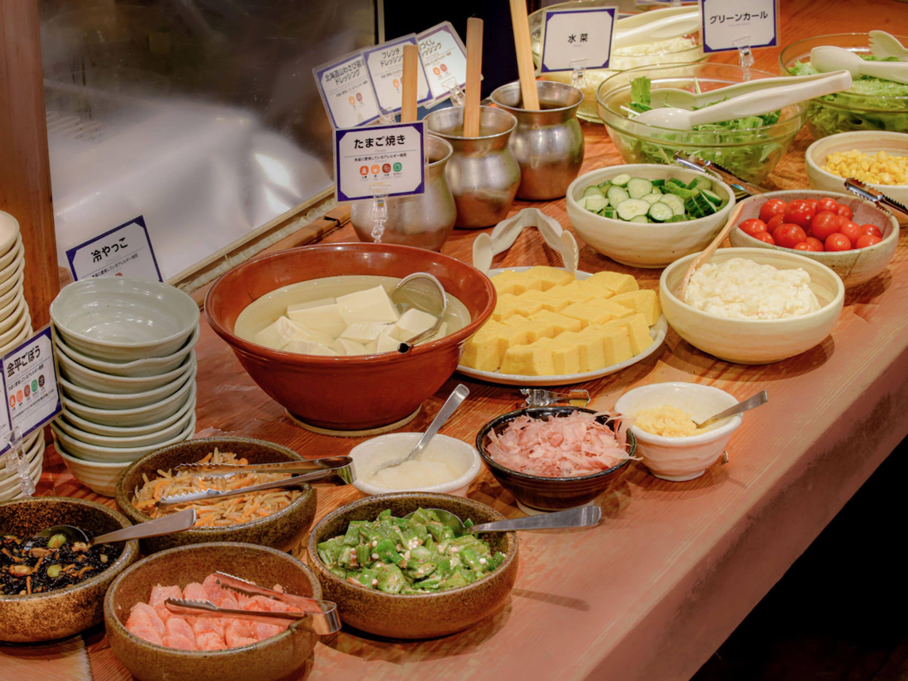 Ein reichhaltiges Buffet mit verschiedenen Speisen, darunter Tofu, Käse, Gemüse und Fleisch.
