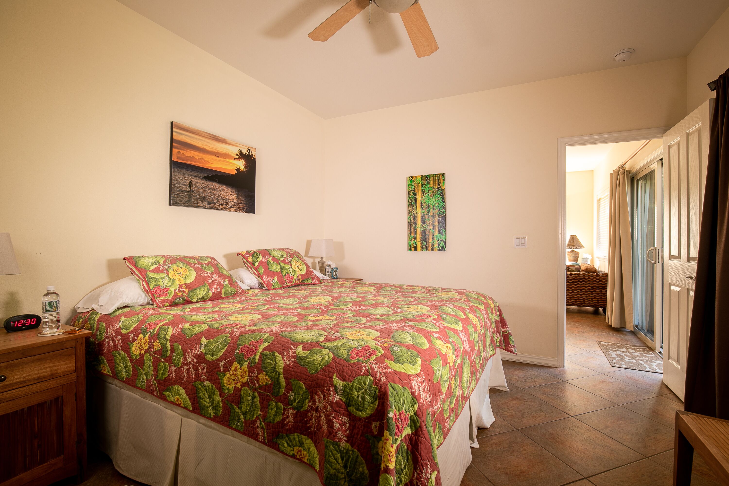 A bedroom with a large bed, a nightstand, a wall clock, and a ceiling fan.
