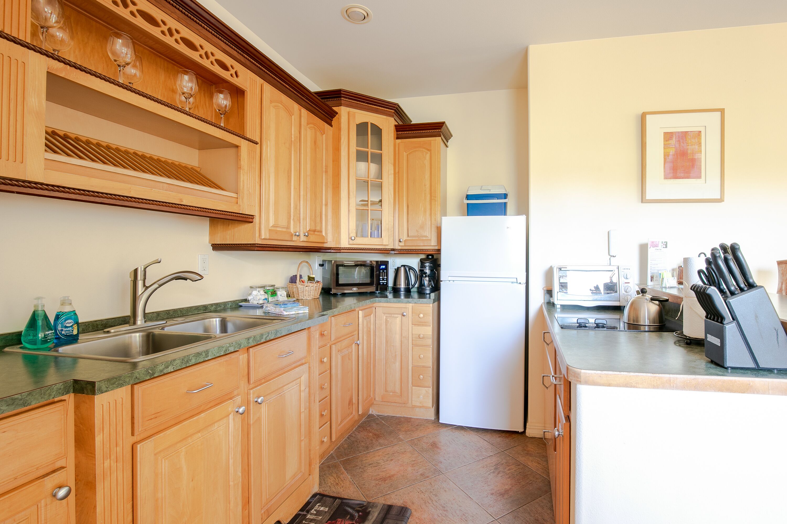 A kitchen with wooden cabinets, a stainless steel sink, a microwave, a refrigerator, and a coffee maker.