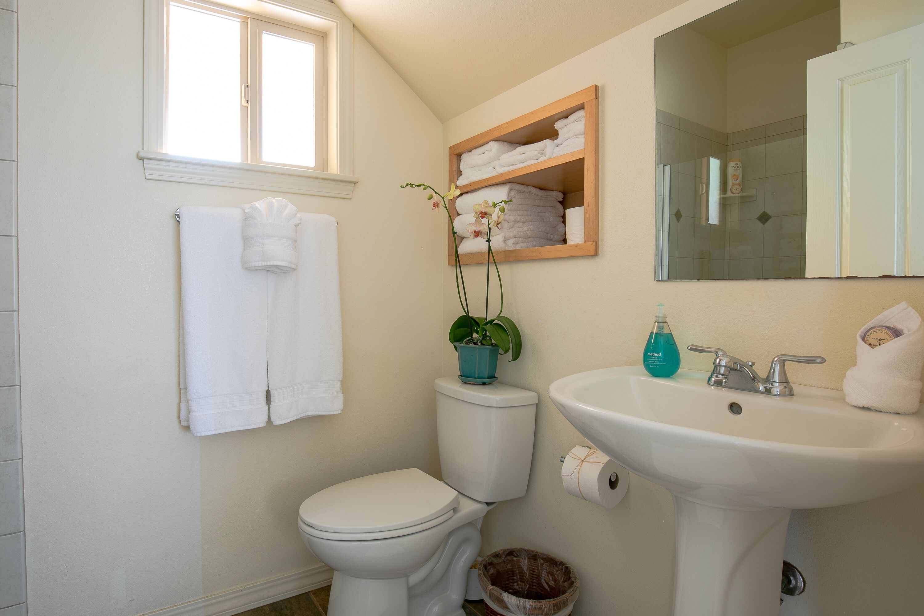 A bathroom with a toilet, sink, and a shelf with towels.