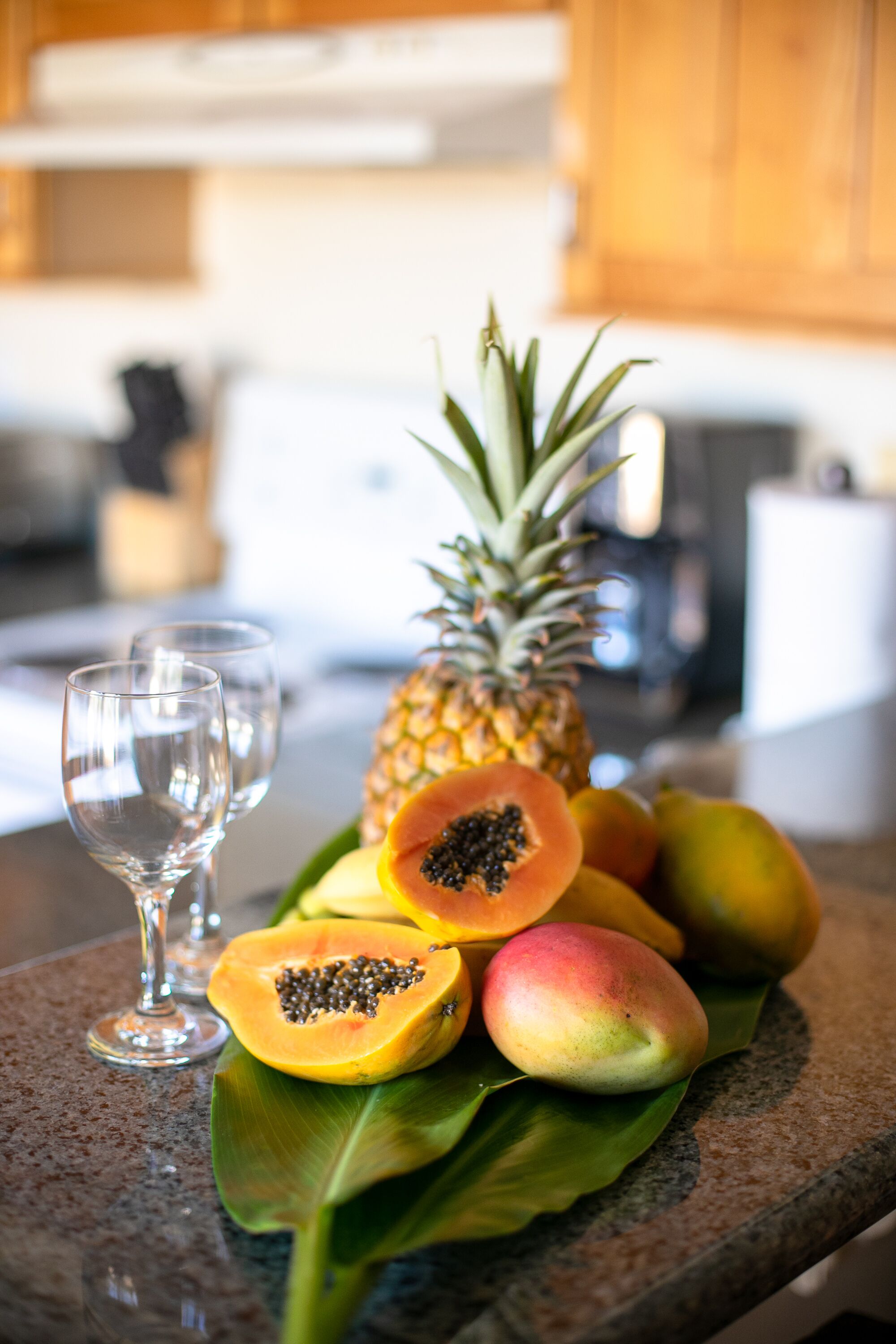 A fruit arrangement on a granite countertop with a pineapple, papaya, and mangoes.
