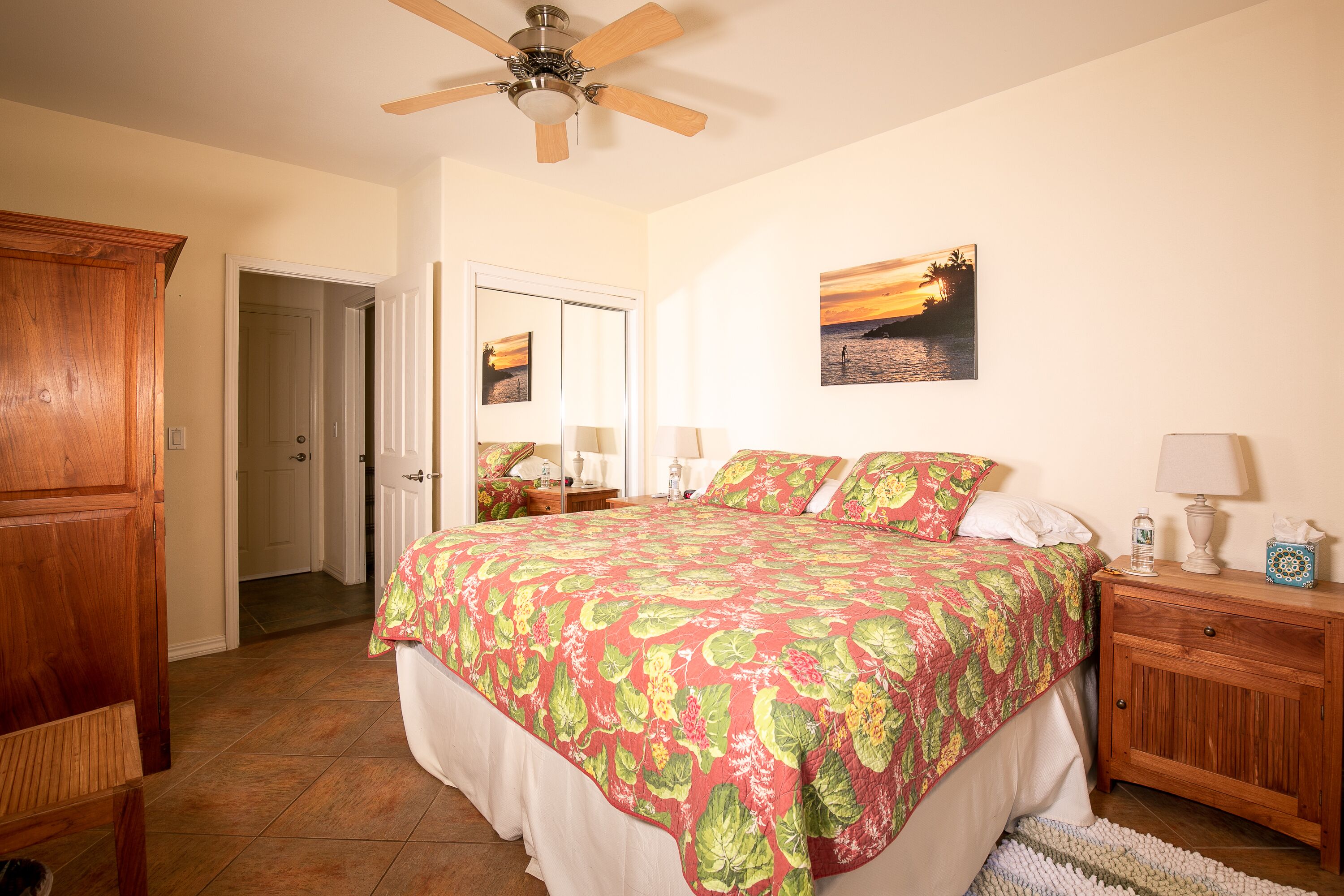 A bedroom with a bed, a wooden nightstand, a ceiling fan, and a door leading to another room.