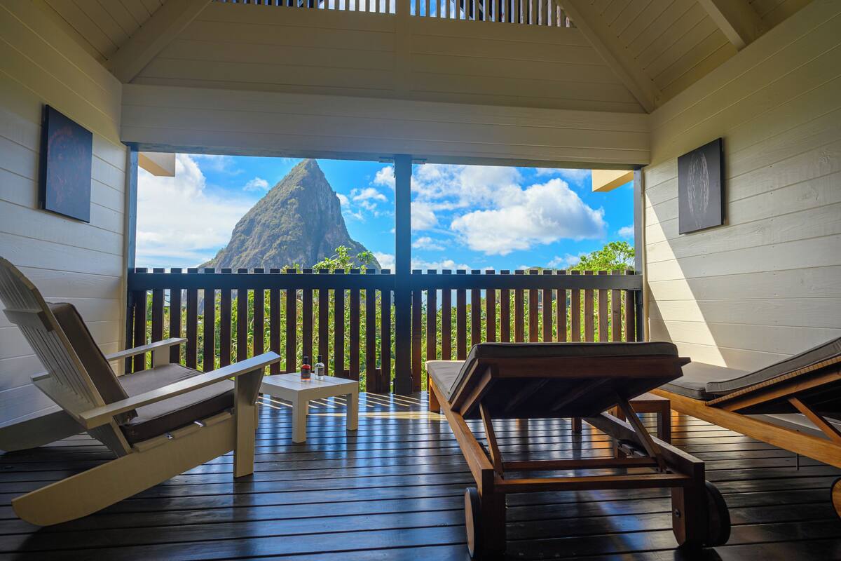 Una terraza de madera con sillones y una mesa, con vistas a una montaña y un cielo despejado.