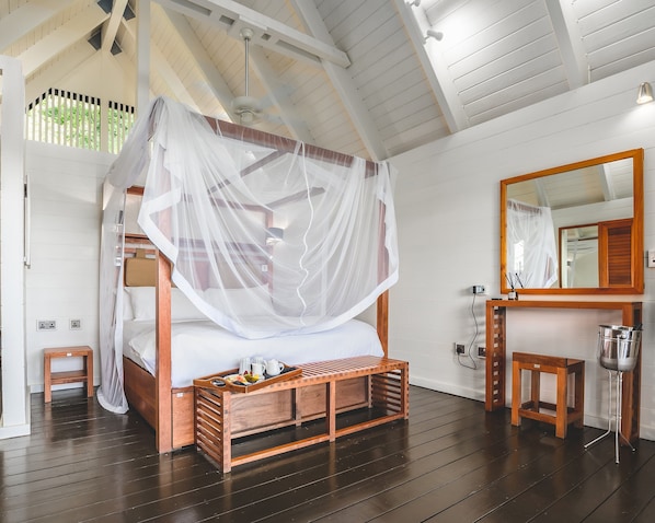 Un dormitorio con una cama de madera, una mesita de noche, un banco de madera y un espejo, además de un ventilador de techo.