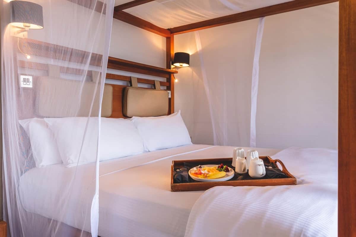 Una habitación de hotel con una cama, una bandeja con artículos de desayuno y una mesita de noche con una lámpara.