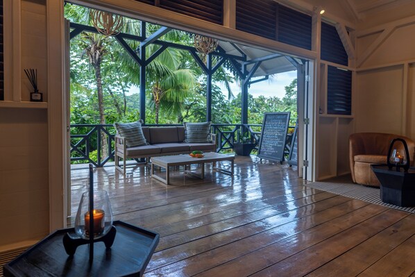 A wooden deck with a sofa, coffee table, and chairs, overlooking a lush garden. - Rabot Hotel from Hotel Chocolat (Soufrière)