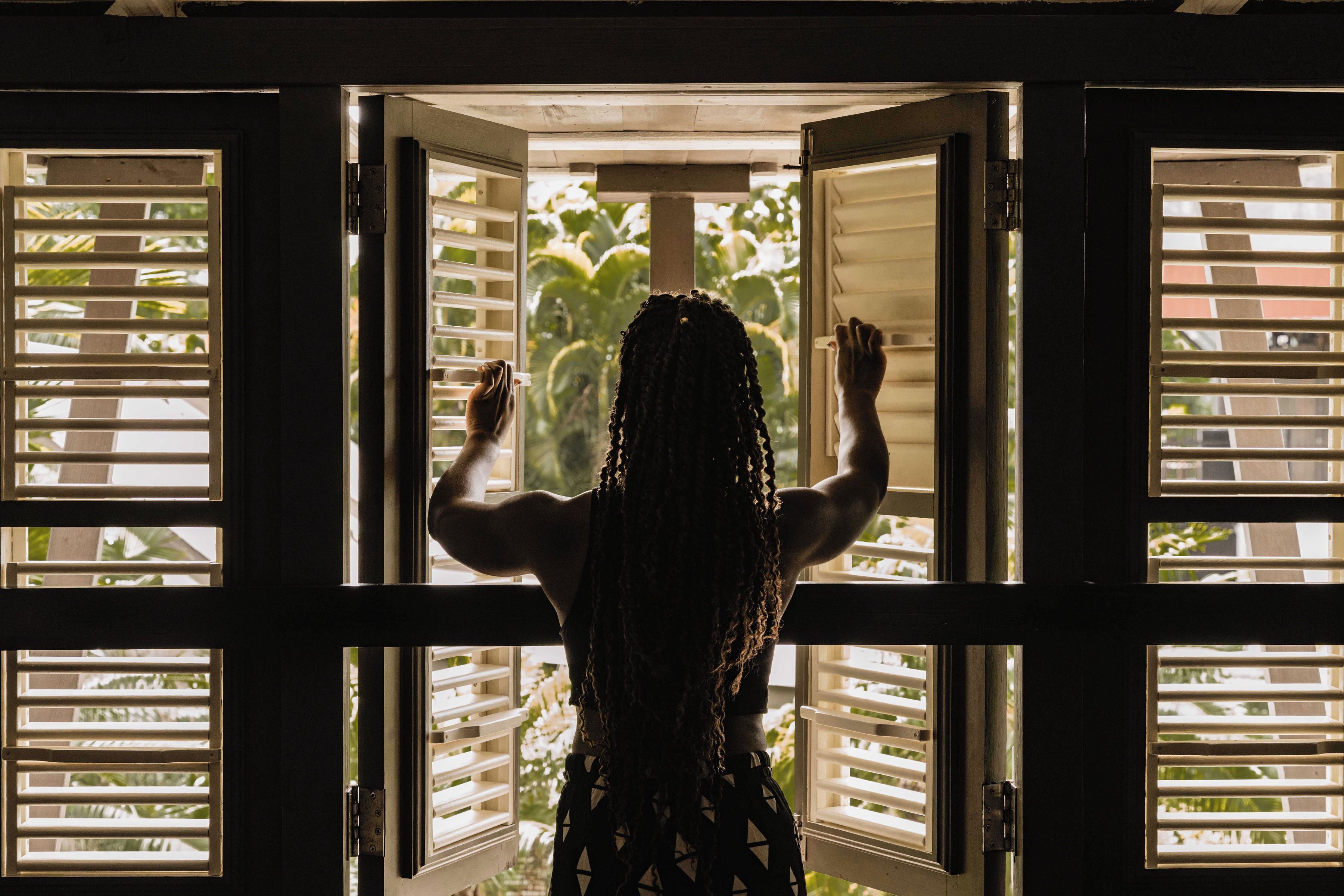 A person standing at an open door with horizontal blinds, looking outside.