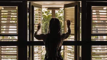 A person standing at an open door with horizontal blinds, looking outside.