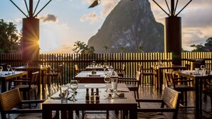 Un restaurante al aire libre con mesas preparadas para comer, una vista de montaña al fondo y una valla de madera que separa el área de comedor del paisaje.