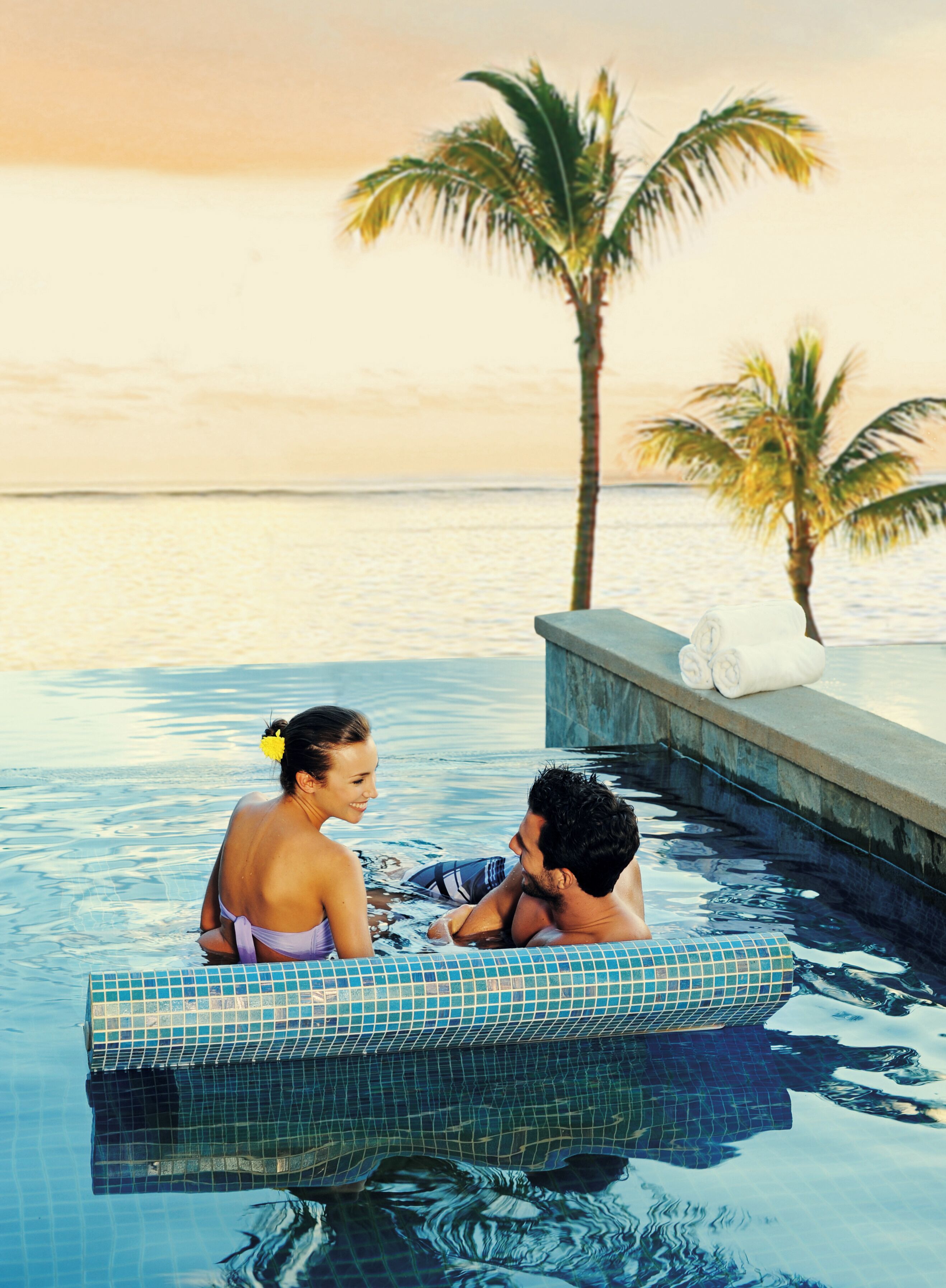 Una pareja en una piscina infinita privada con vista al océano y palmeras.