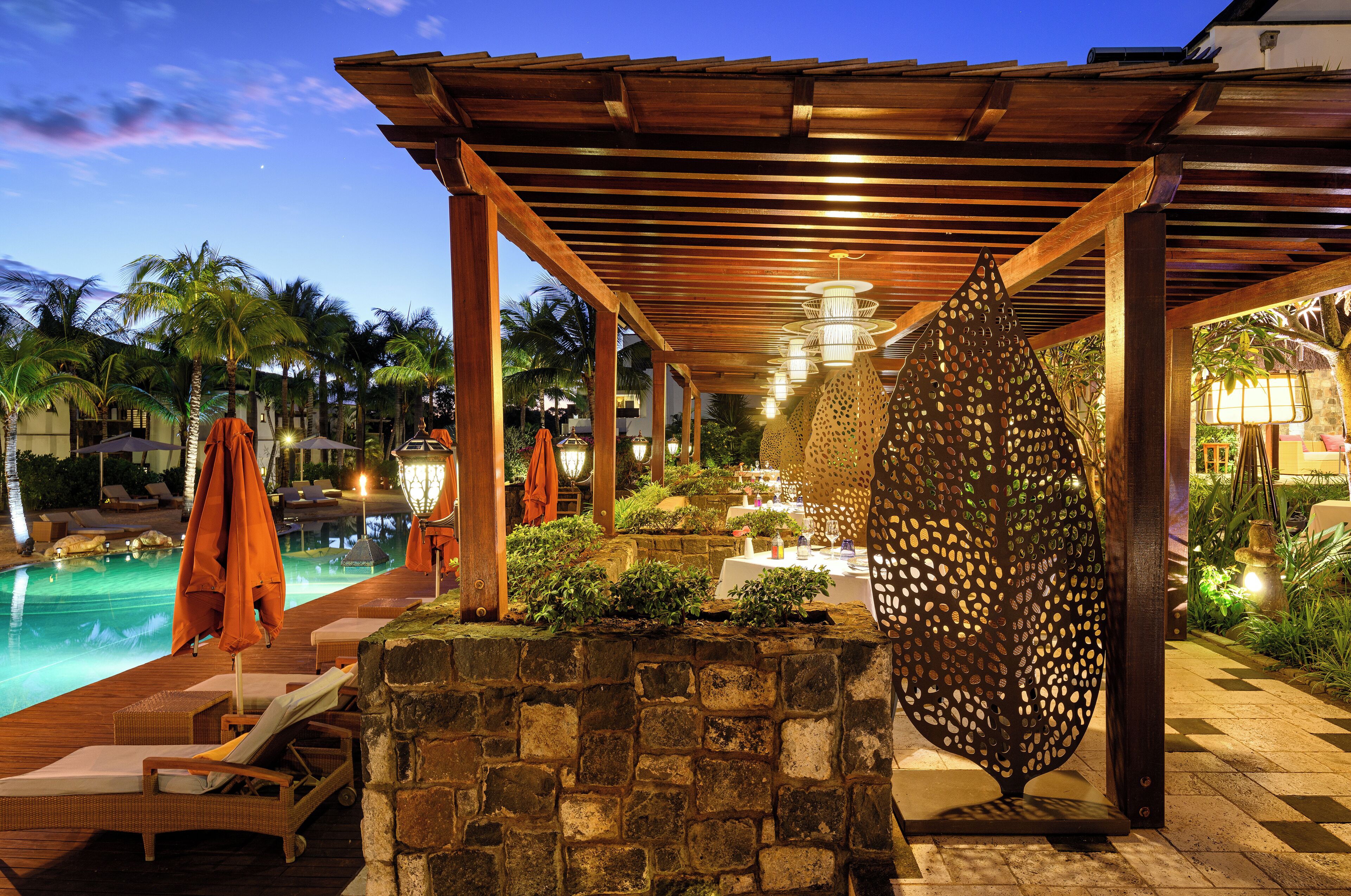 A covered pool area with lounge chairs, a stone wall, and a decorative metal screen.