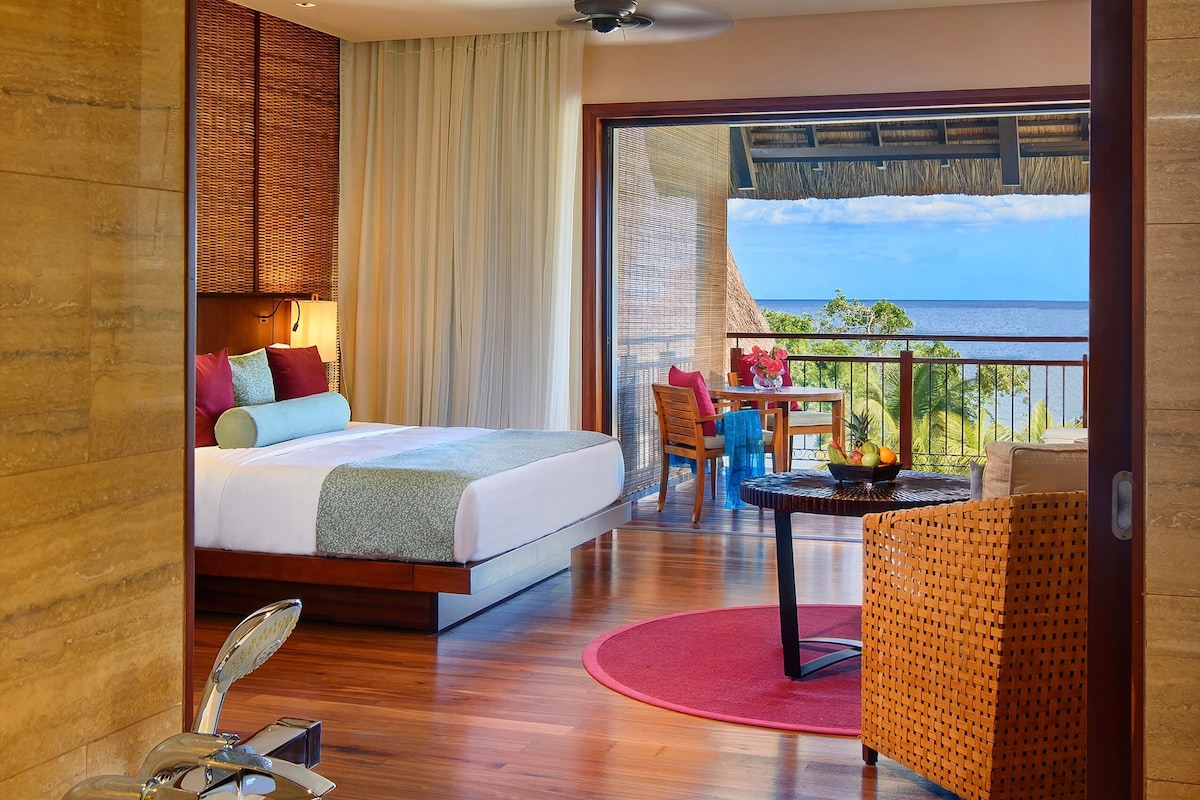 A hotel room with a bed, a balcony with a view, a bathroom with a bathtub, and a dining area.