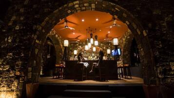 Un intérieur agrémenté d’une arche en pierre, d’un bar avec des tabourets et d’un plafond orné de luminaires suspendus.