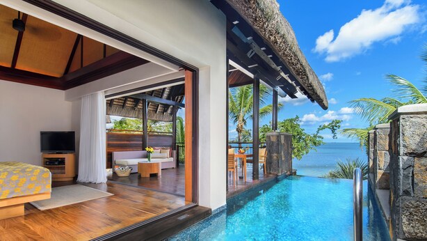 Une chambre d’hôtel moderne dotée d’une grande baie vitrée donnant sur une piscine et l’océan.